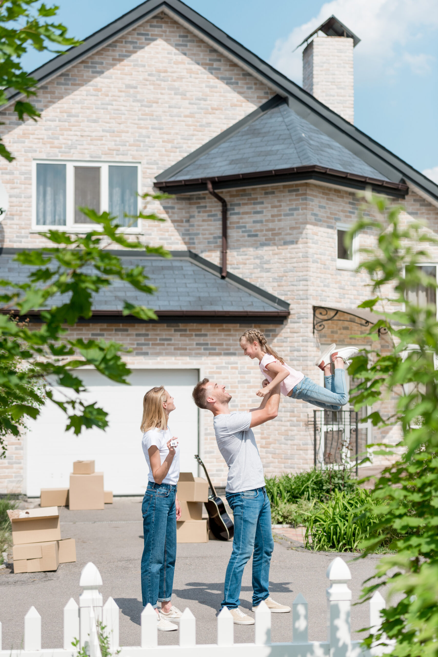 side view of father raising up daughter while mother standing near in front of their new house